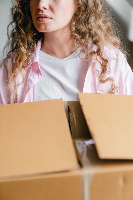Inside a storage area with a white brick wall and metal shelving unit used for house removals and packing, there are multiple cardboard boxes of varying sizes, some labeled as fragile and sealed with